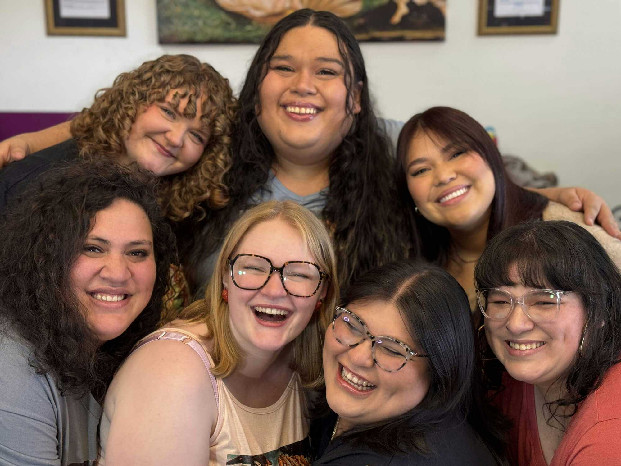 Group of seven smiling people posing together indoors.